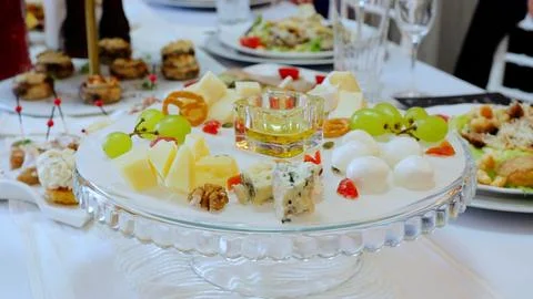 Crystal serving platter displaying an assortment of cheeses, fresh green grapes Stock Photos