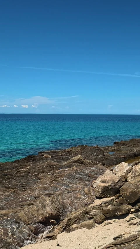 Crystal waters meet rugged rocks under clear skies. Lagomandra, Greece. Vertical Stock-Footage 339626407