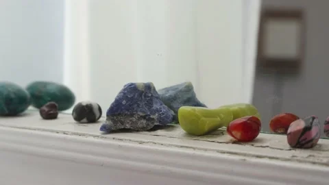Crystals and gemstones lined up on window sill with white sheer curtain Vídeos de archivo 233659043