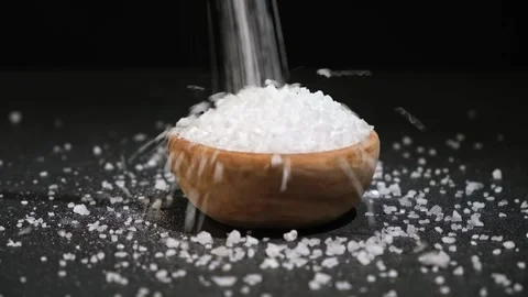 Crystals of table salt are poured into wooden bowl on a black background. Coarse Stock Footage 239682768