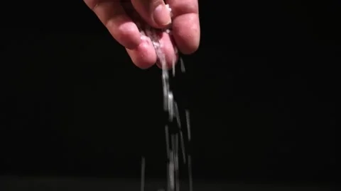 Crystals of table salt fall from the fingers of the hand on black background Stock Footage 240396200