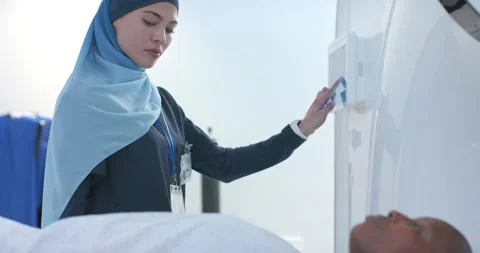 CT tech is pressing controls, sliding patient into gantry while red lasers are Stock Footage 336535853