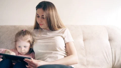 CU, 4k: Young attractive mother and sweet daughter are sitting on the couch and Stock Footage 105115697