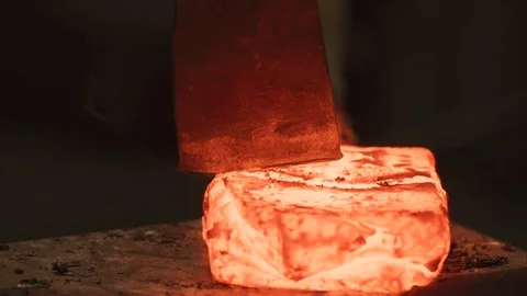 CU of axe cutting red hot ingot by Master Sword smith. Traditional Forge Stock Footage 125435079