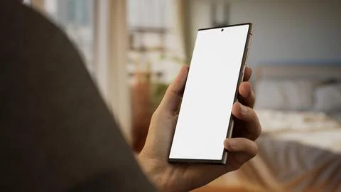 CU Caucasian man using his generic phone, morning bedroom in the background Foto stock