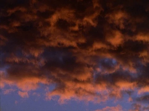 CU of orange and black clouds in blue sky. Pans left to right. Stock Footage 86751237