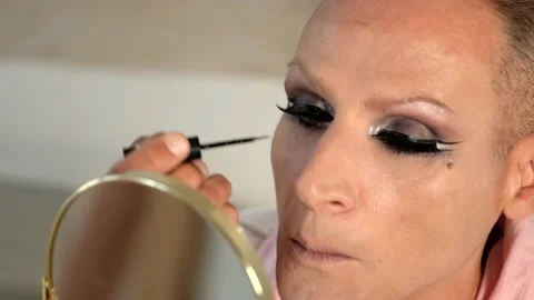CU portrait of travesty looking at mirror and applying eyeliner with a brush Stock Footage 161834186