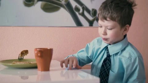 CU: Schoolboy sits at the table in school uniform and has breakfast, playing Stock Footage 105096335