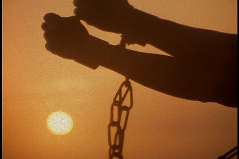 CU silhouette of chained arms raised to the sun against a dark orange sky. Stock-Footage 86751471