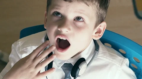 CU, Slow motion: schoolboy sits at table in school uniform and yawns while doing Stock Footage 105095959