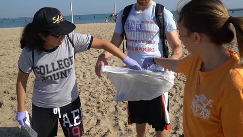 CU OF YOUNG ADULTS PUTTING BEACH DEBRIS IN COLLECTION BAGS Stock Footage 128333231