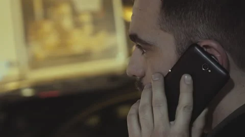CU young man speaking on the phone at night outside on busy city street Stock Footage 60554103