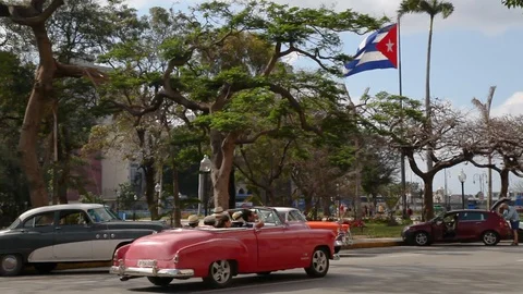 Cuban flag blowing in the breeze with old 1950s cars driving by in Old Havana Stock Footage 90918232