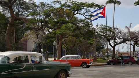 Cuban flag blowing in the breeze with old 1950s cars driving by in Old Havana Stock Footage 90918357