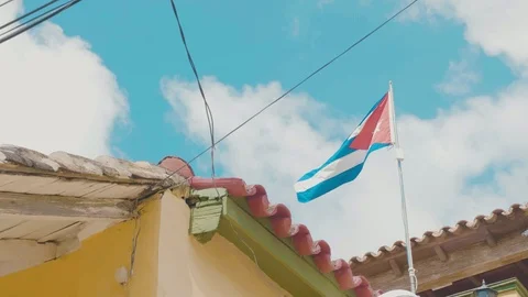 Cuban flag flaps in the wind on a colourful building against a sunny blue sky Stock Footage 88764708