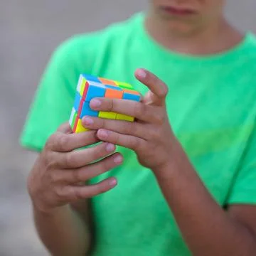 Cube puzzle with multi-colored faces in the hands of a child of school age Stock Photos