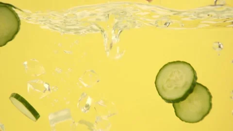Cucumber slices and ice cubes falling into a water isolated on yellow background Stock-Footage 153479464