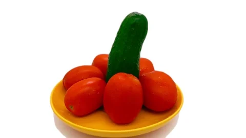A cucumber stands surrounded by a tomato on a yellow saucer and rotates on a Stock Footage 117636819