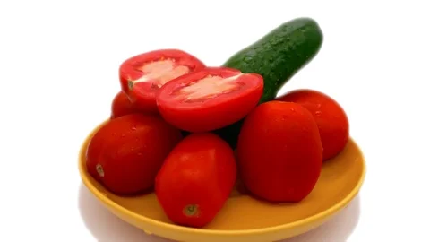 A cucumber stands surrounded by a tomato on a yellow saucer and rotates on a Video stock 117636857