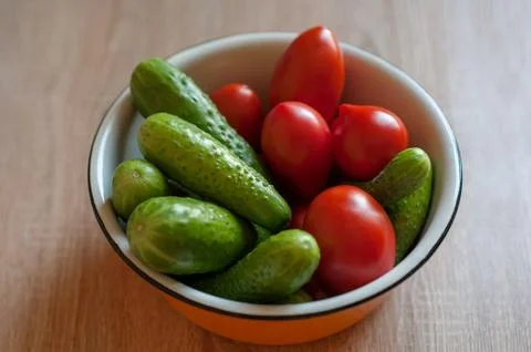 Cucumbers and tomatoes in a cup on the table Stock Photos