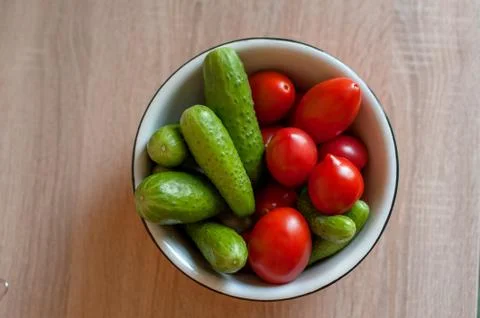 Cucumbers and tomatoes in a cup on the table Stock Photos
