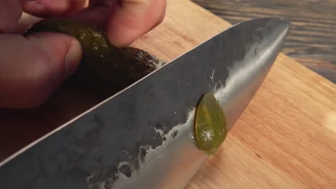 Cucumbers are cut with a knife on the board for the homemade grilled burger Stock Footage 148875397
