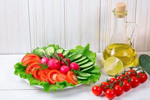 Cucumbers, radish, tomatoes cherry, olive oil, herb and spices on old white.. Stock Photos