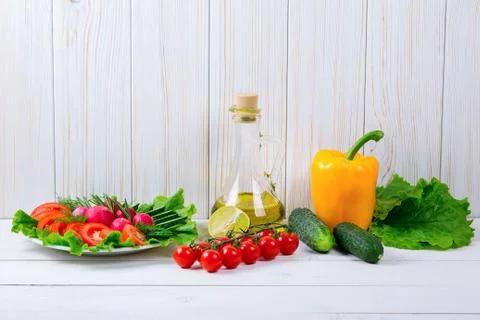 Cucumbers, radish, tomatoes cherry, olive oil, herb and spices on old white w Stock Photos