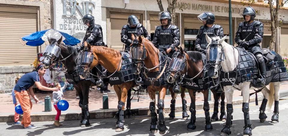 Cuenca, Ecuador - August 13, 2015 - Small girl looks up at a line of police on Stock Photos