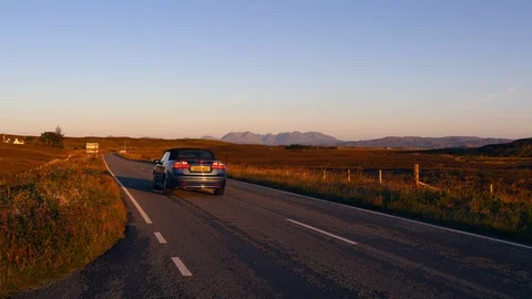 Cuillin Hills seen from far at sunset with two cars crossing by the road Stock Footage 97524218