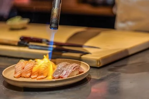 Culinary artist using torch to sear sushi on plate in modern kitchen Stock Photos