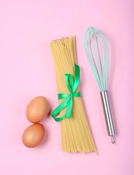 Culinary concept, cooking process. Pasta, chicken eggs, whisk on pink backgro Stock Photos