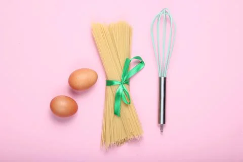 Culinary concept, cooking process. Pasta, chicken eggs, whisk on pink backgro Stock Photos
