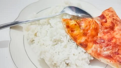 A culinary experiment: a slice of pizza on a plate of rice 스톡 사진