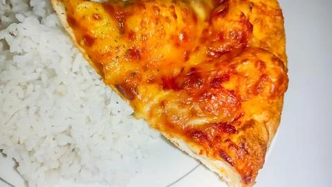 A culinary experiment: a slice of pizza on a plate of rice 스톡 사진