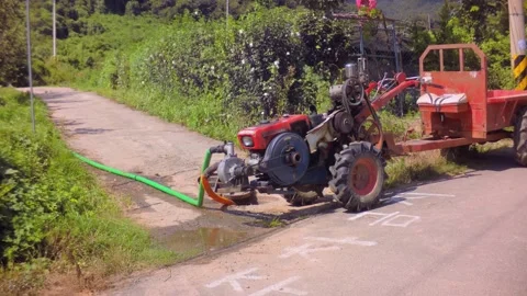 Cultivator engine connected to a water pump pumping water on a rural road in Sou Stock Footage 340579764
