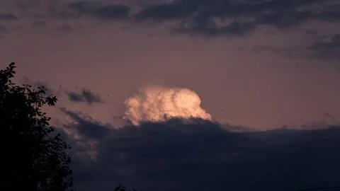 Cumulus cloud in the golden rays of the sunset over the dark horizon with Stock Photos