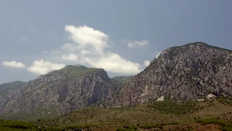 Cumulus clouds drift above forested mountains, framing rocky peaks and green Vídeos de archivo 333757759