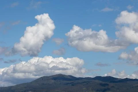 Cumulus clouds drifting over rolling hills on sunny day Stock Photos
