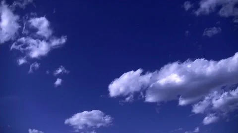 Cumulus clouds float across a clear blue sky Stock Footage 129691531