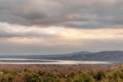 Cumulus clouds float over a serene lake with mountains in the background Stock Photos
