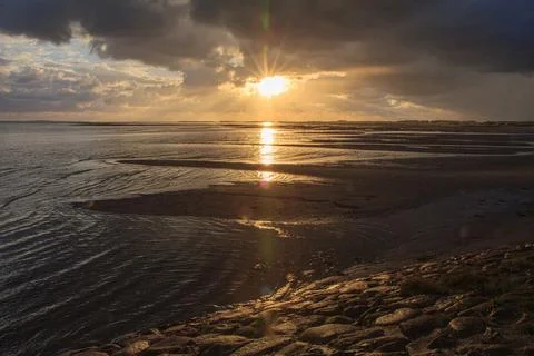 Cumulus clouds float in the sky as the sun sets over the tranquil water at dusk Stock Photos