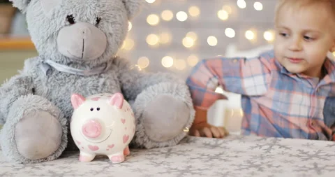 The cunning boy sits at the table and touches the piggy bank. Stock Footage 140157886