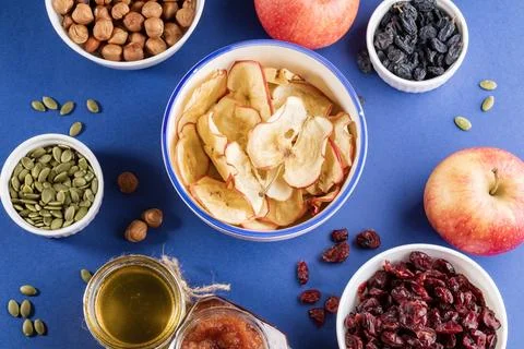 Cup with apple chips surrounded by healthy snacks on blue bright background. Stock Photos