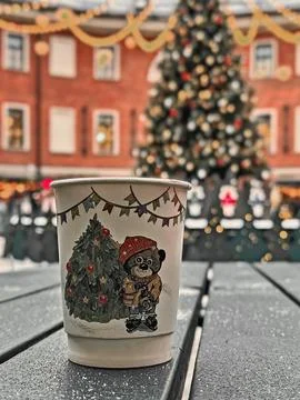 Cup with a bear on it sits on a table next to a Christmas tree. Stock Photos