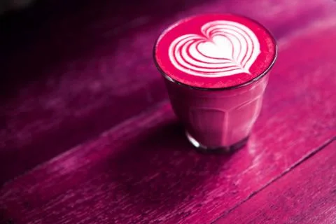 Cup of beetroot latte coffee is on the painted table background Stock Photos