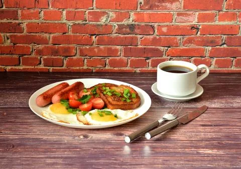 A cup of black coffee and two fried eggs with sausages, toast and cherry to.. Stock Photos