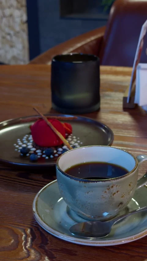 Cup black coffee beside plated dessert on wooden cafe table with warm indoor Stock Footage 345765269