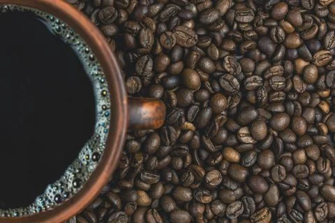 Cup of black coffee with frothy bubbles surrounded by coffee beans Stock Photos