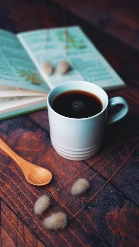 Cup of black coffee with an open book and wooden spoon on a rustic wooden table Video stock 343471596